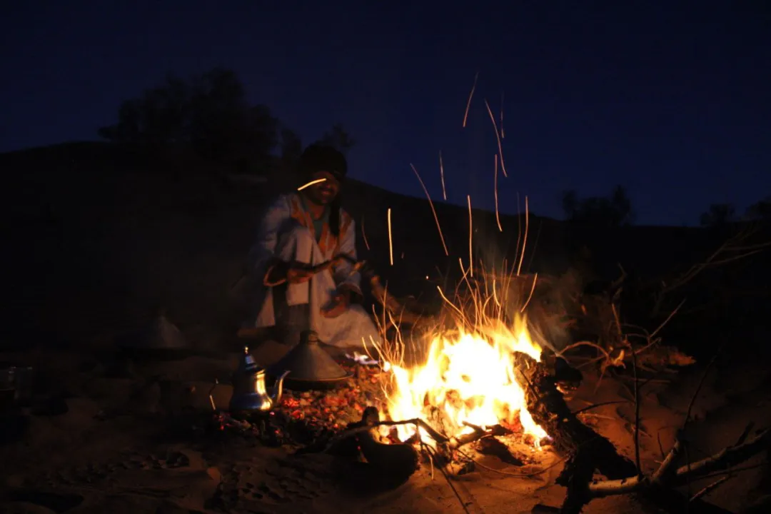 A group of people sitting around a campfire in the desert at night