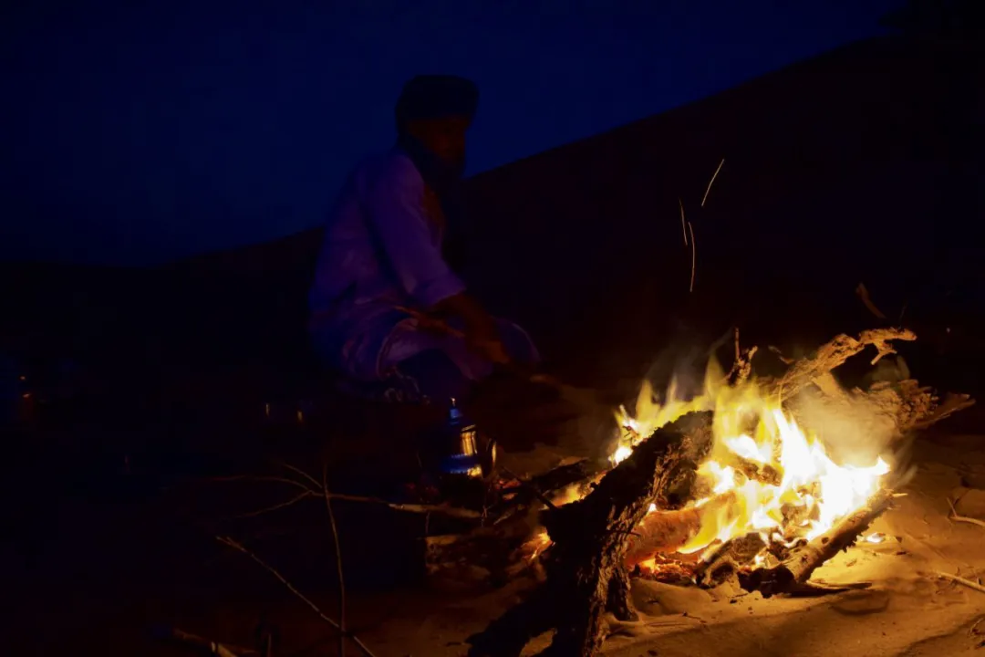 A person standing on a dune, looking out at the vast desert landscape during sunset