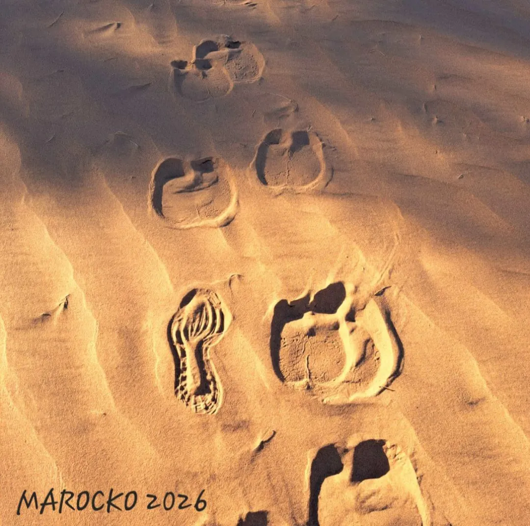 A lone person walking across desert dunes with a clear sky above, emphasizing solitude and vastness.