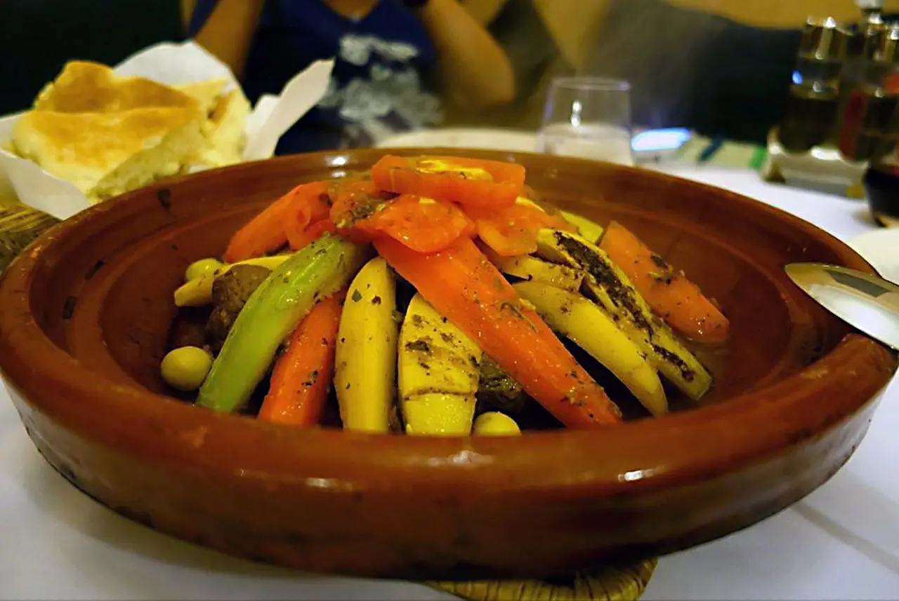 A traditional Moroccan tagine with meat and arranged vegetables like carrots, potatoes, and zucchini in a clay pot.