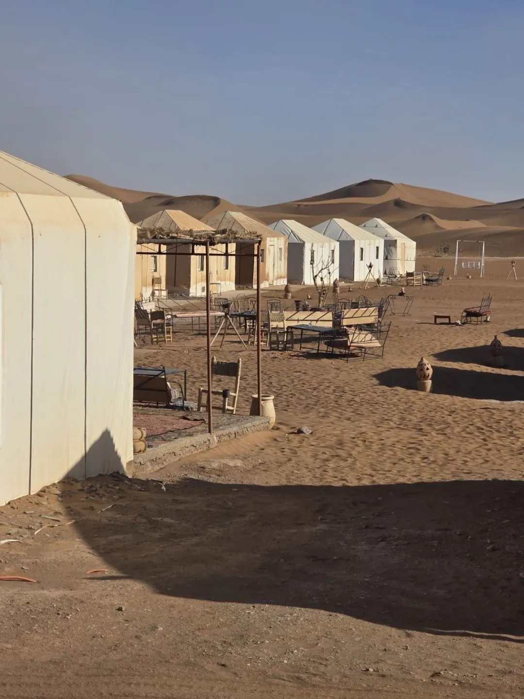 Desert camp with white tents and outdoor seating among sand dunes
