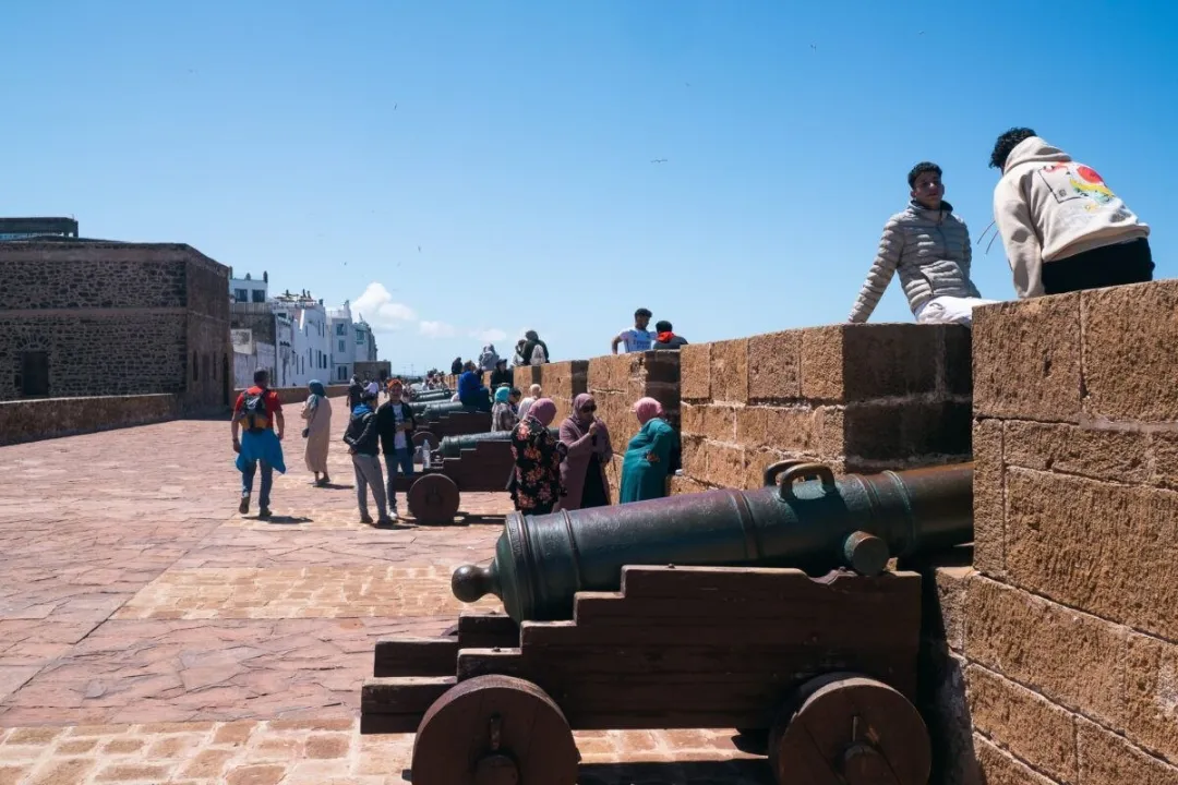 Historic cannons on a stone rampart with visitors under a clear blue sky