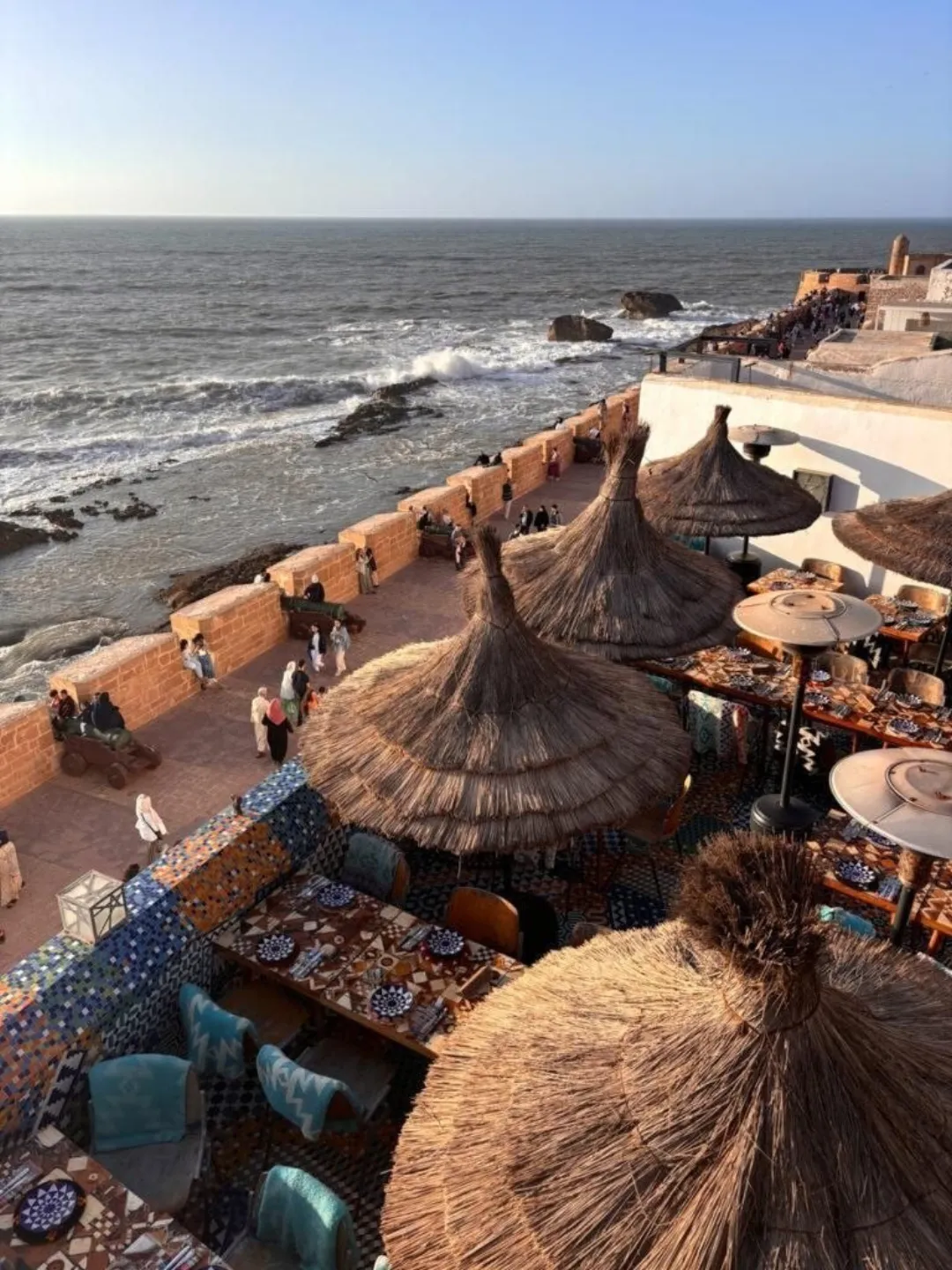 Seaside terrace with thatched umbrellas overlooking waves and rocky coast