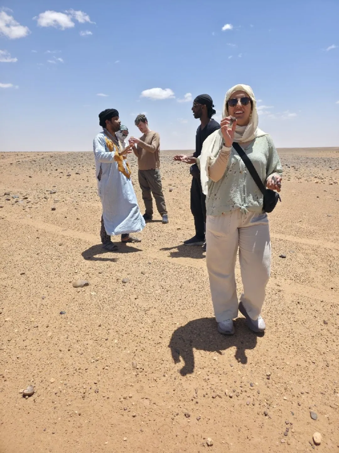 Travelers examine stones on a rocky desert plain under a blue sky