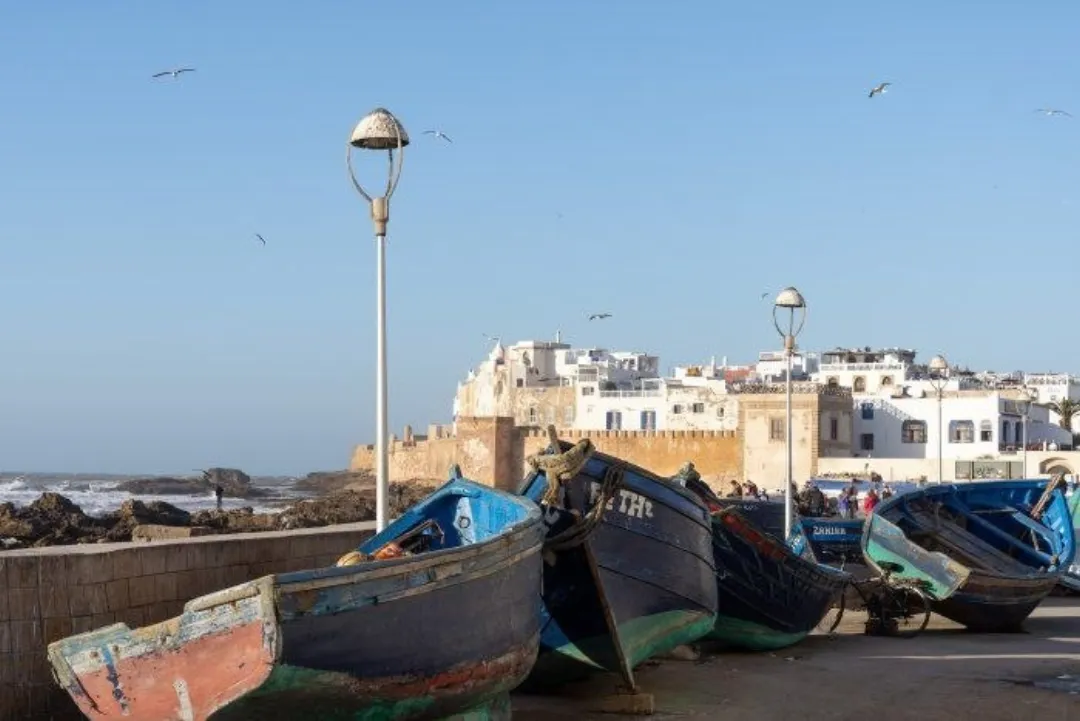 Weathered blue fishing boats beside a coastal walled town under a clear sky