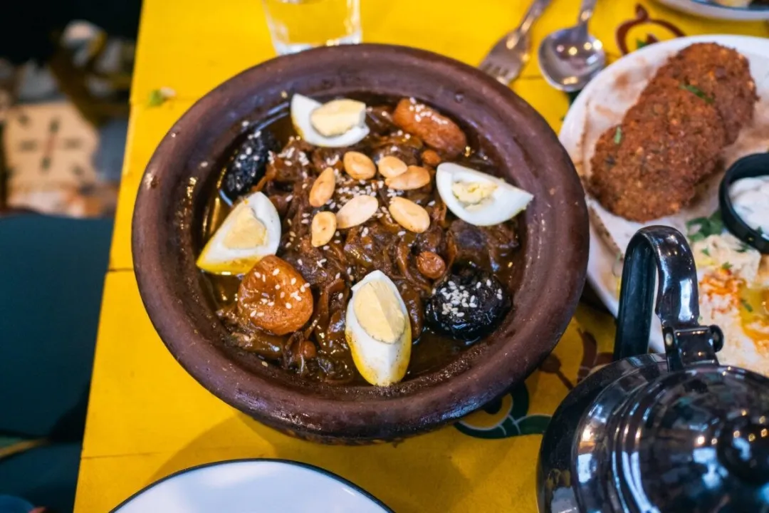 Clay tagine with stewed meat, boiled eggs, dried fruit and almonds on a yellow table