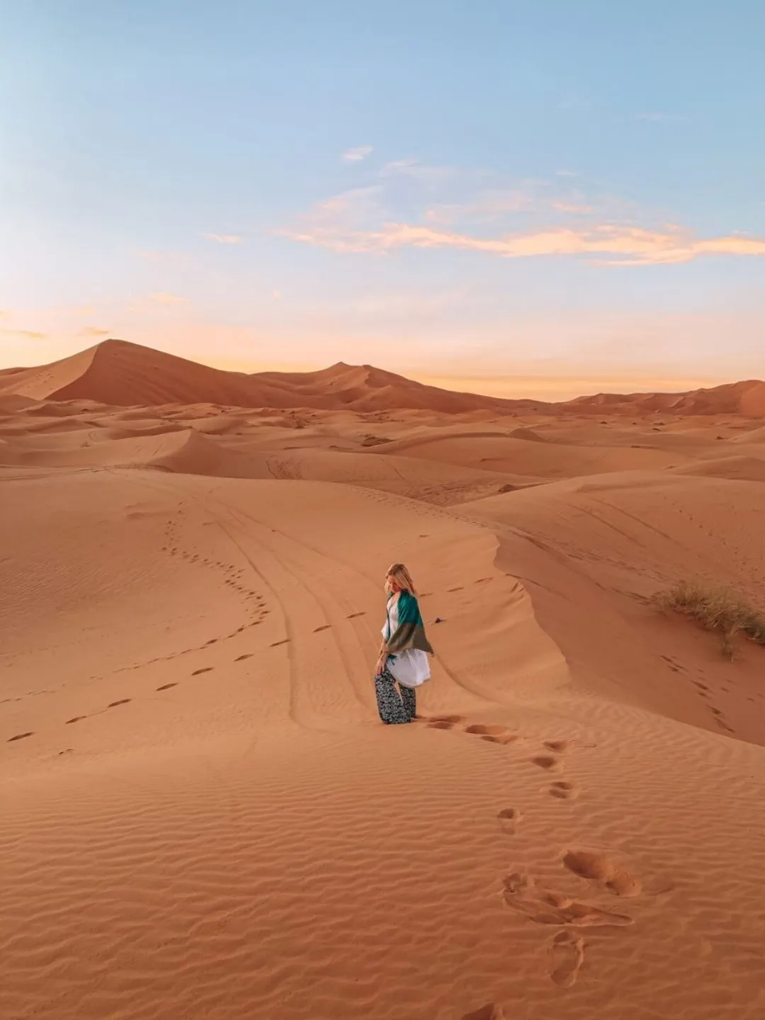 Person walking among orange Sahara dunes at sunset