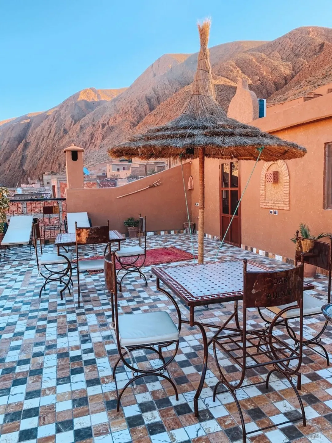 Tiled rooftop terrace with metal chairs, straw parasol, and rocky desert mountains