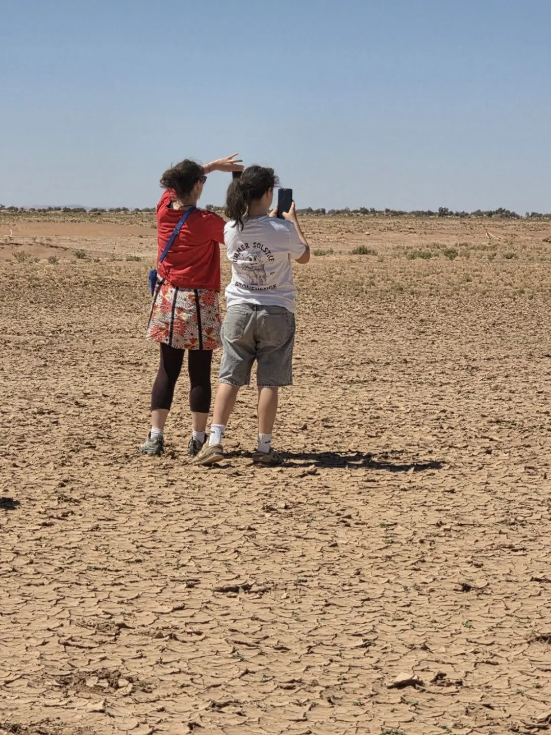 Two travelers photographing a dry cracked desert landscape under a clear sky