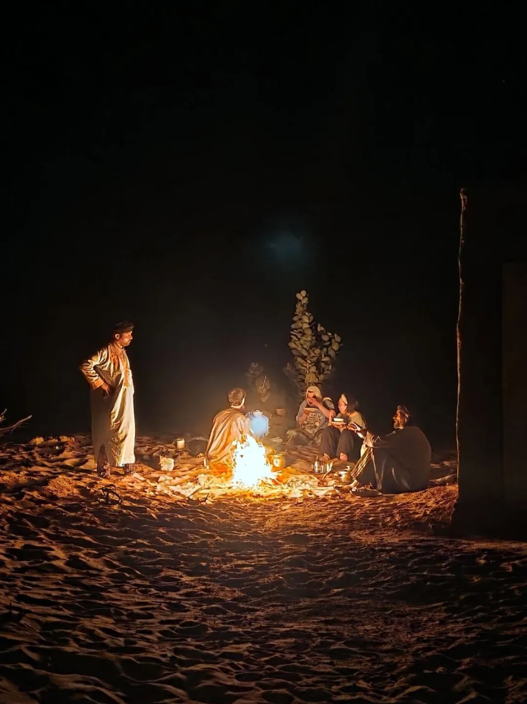 People gathered around a campfire on desert sand at night