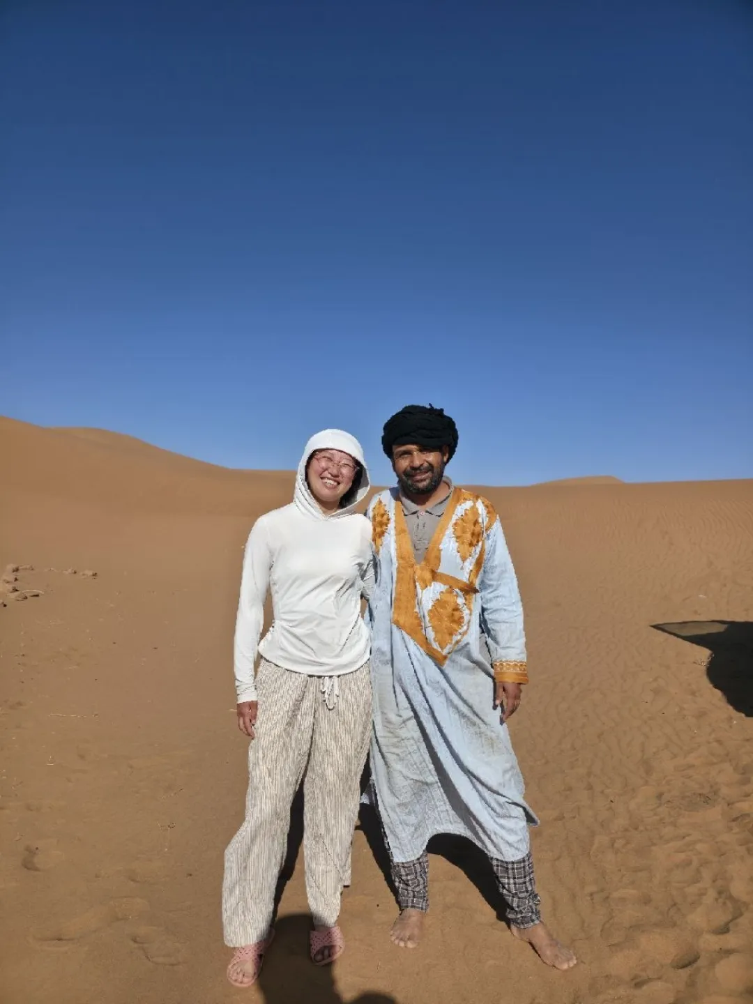 Two people posing together on desert sand dunes under a clear blue sky